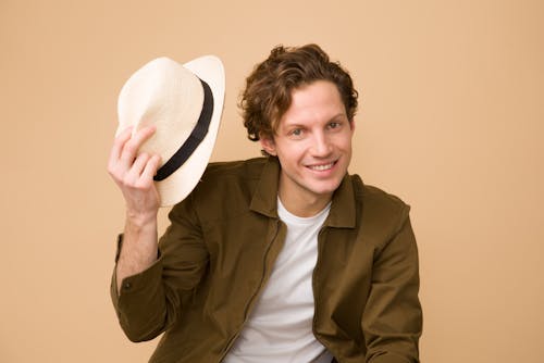 無料 白いfedora帽子を保持している茶色のドレスシャツを着ている男 写真素材